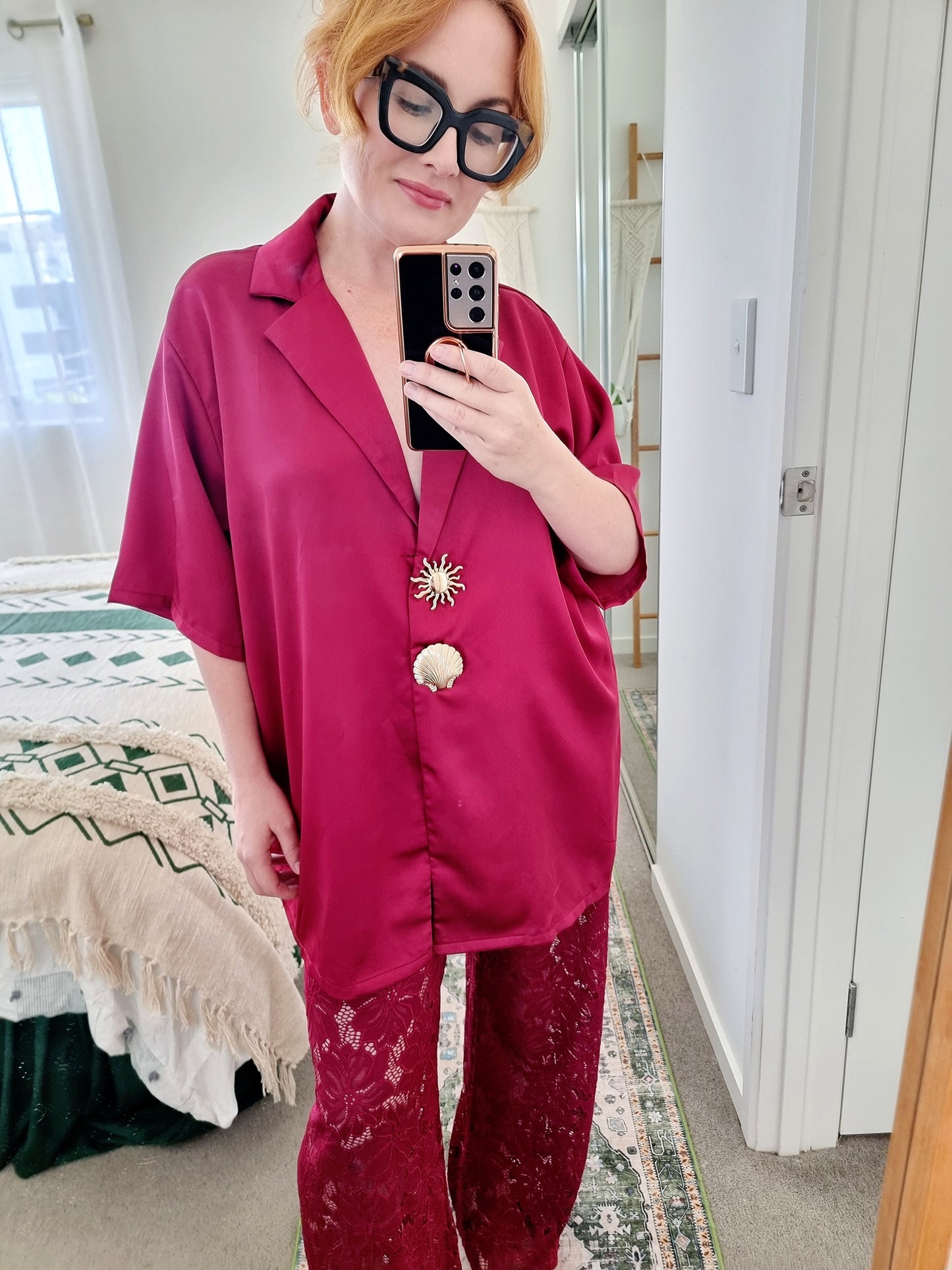 Tegan wearing the Amara Set in Merlot by By Frankie. Oversized satin shirt with statement shell and sun buttons, paired with sheer burgundy lace pants. Tegan is an AU size 10 and wears the Medium.