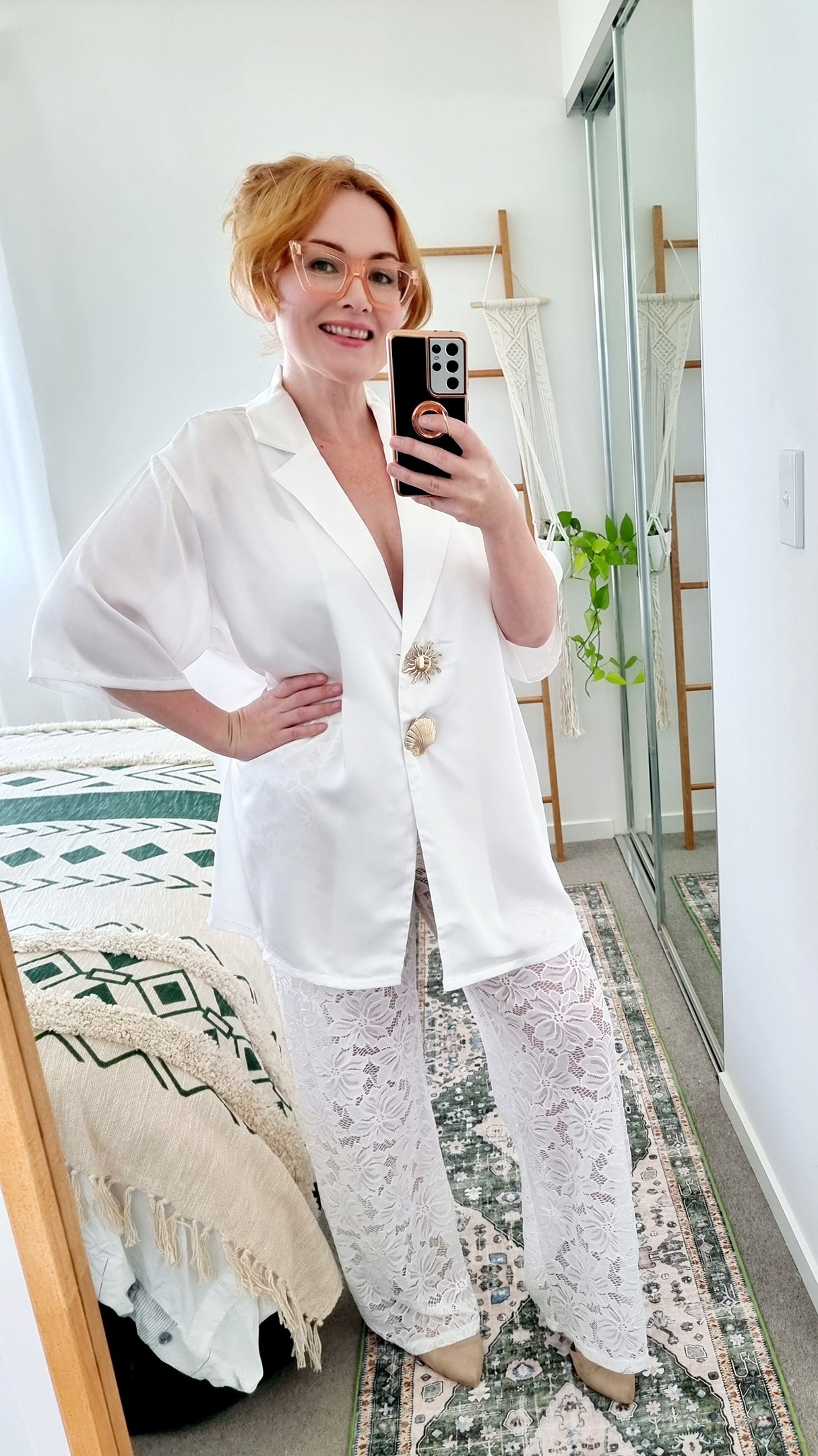 Tegan wearing the Amara Set in White by By Frankie. Oversized white satin shirt with gold shell and sun buttons, styled with sheer white floral lace pants. Tegan is an AU size 10 and wears the Medium.