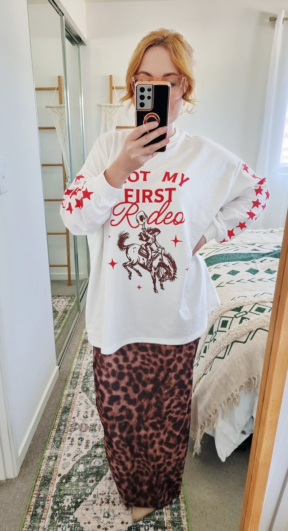 Tegan wearing the Not My First Rodeo Set by By Frankie in size Medium. Features a white oversized sweatshirt with red rodeo graphic and star-print sleeves, paired with a brown leopard-print mesh skirt. Tegan is AU size 10.