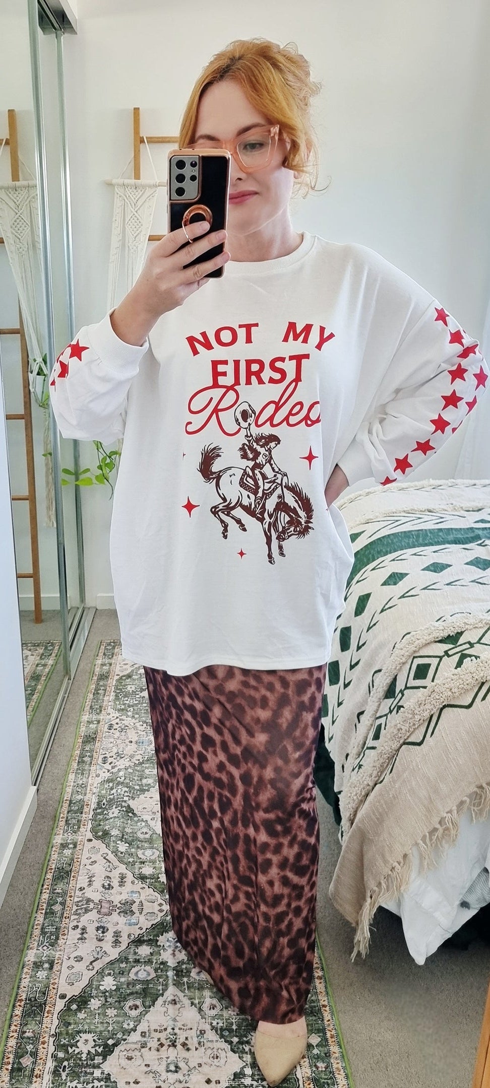 Tegan wearing the Not My First Rodeo Set by By Frankie in size Medium. Features a white oversized sweatshirt with red rodeo graphic and star-print sleeves, paired with a brown leopard-print mesh skirt. Tegan is AU size 10.