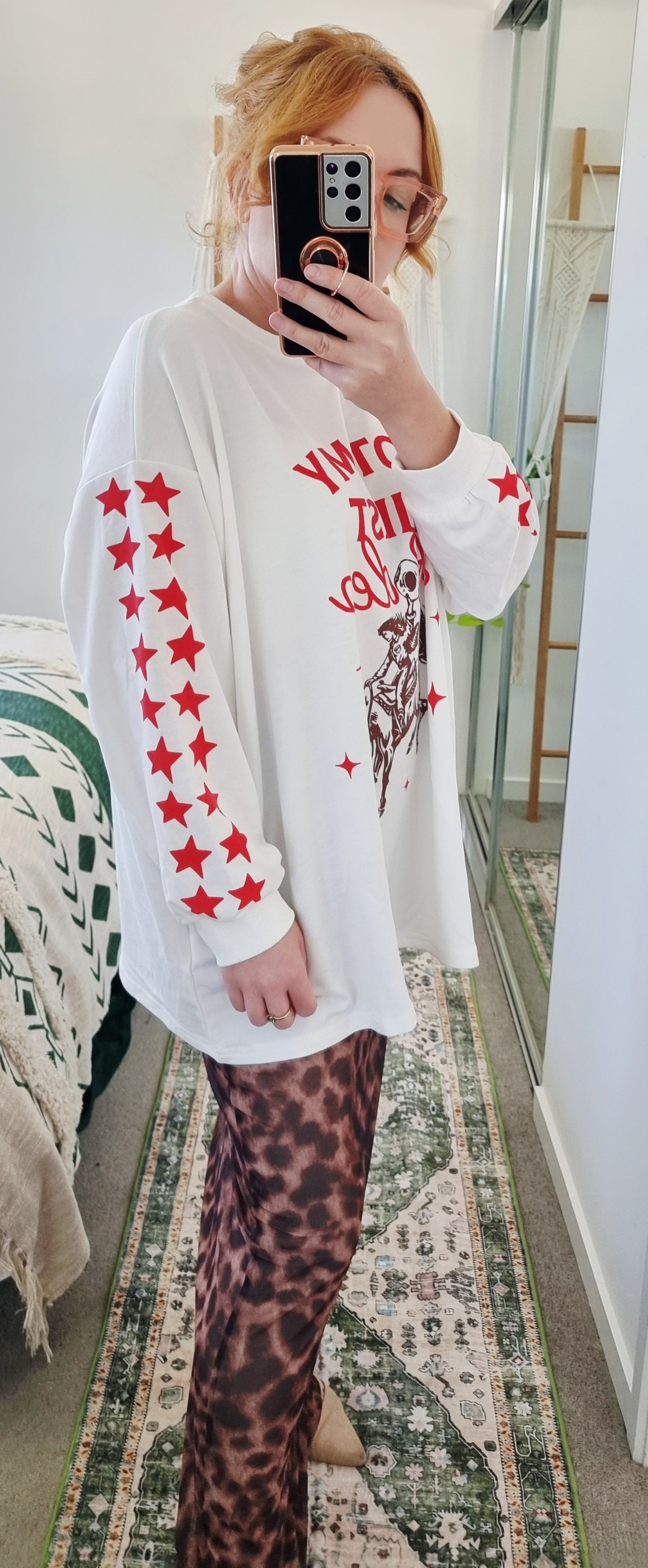 Tegan wearing the Not My First Rodeo Set by By Frankie in size Medium. Features a white oversized sweatshirt with red rodeo graphic and star-print sleeves, paired with a brown leopard-print mesh skirt. Tegan is AU size 10.