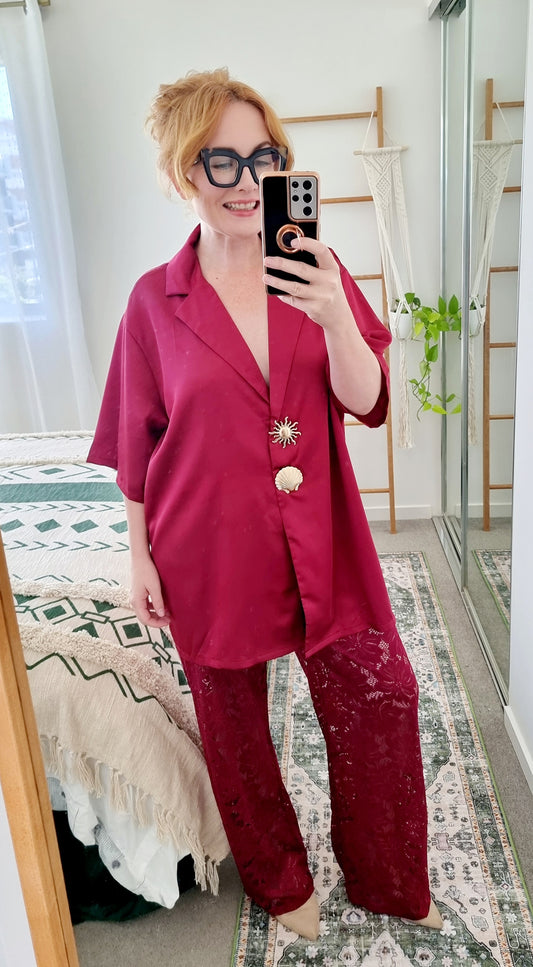 Tegan wearing the Amara Set in Merlot by By Frankie. Oversized satin shirt with statement shell and sun buttons, paired with sheer burgundy lace pants. Tegan is an AU size 10 and wears the Medium.