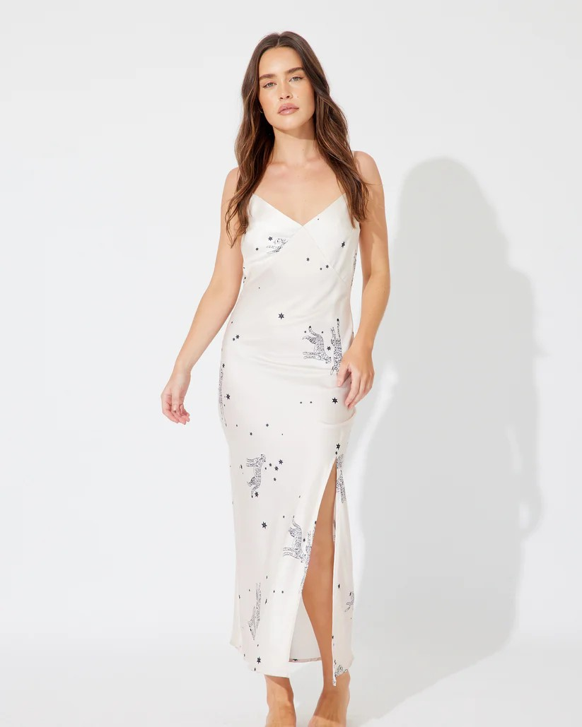 Model wearing the Asteria Dress – cream satin bias-cut maxi with black celestial and leopard print, cowl neckline, and side split.