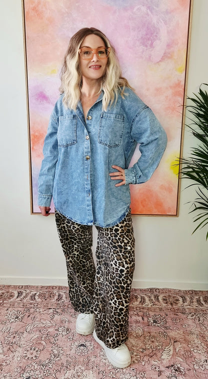 Front view of a light denim oversized shacket with white Western-style illustrations including a snake, flames, dice, and "By Frankie" banner text on the back. Tegan wears the medium and is a size 10 to 12. 