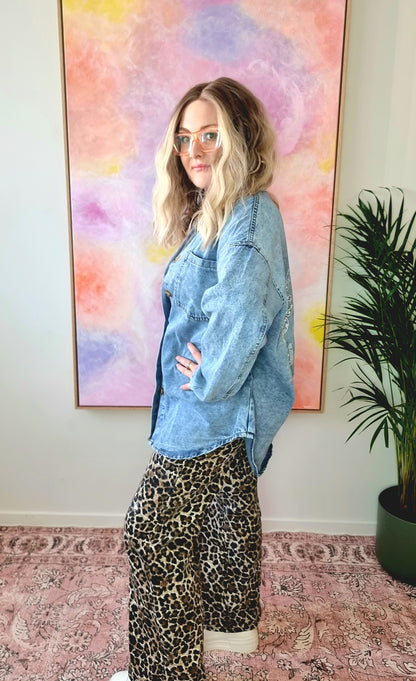 Side view of a light denim oversized shacket with white Western-style illustrations including a snake, flames, dice, and "By Frankie" banner text on the back. Tegan wears the medium and is a size 10 to 12. 