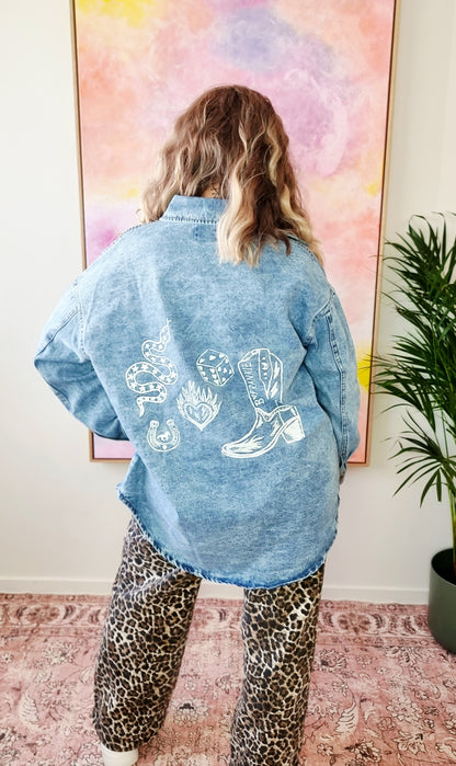 Back view of a light denim oversized shacket with white Western-style illustrations including a snake, flames, dice, and "By Frankie" banner text.
