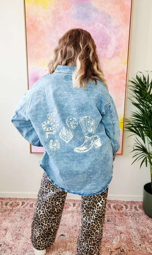 Back view of a light denim oversized shacket with white Western-style illustrations including a snake, flames, dice, and "By Frankie" banner text.