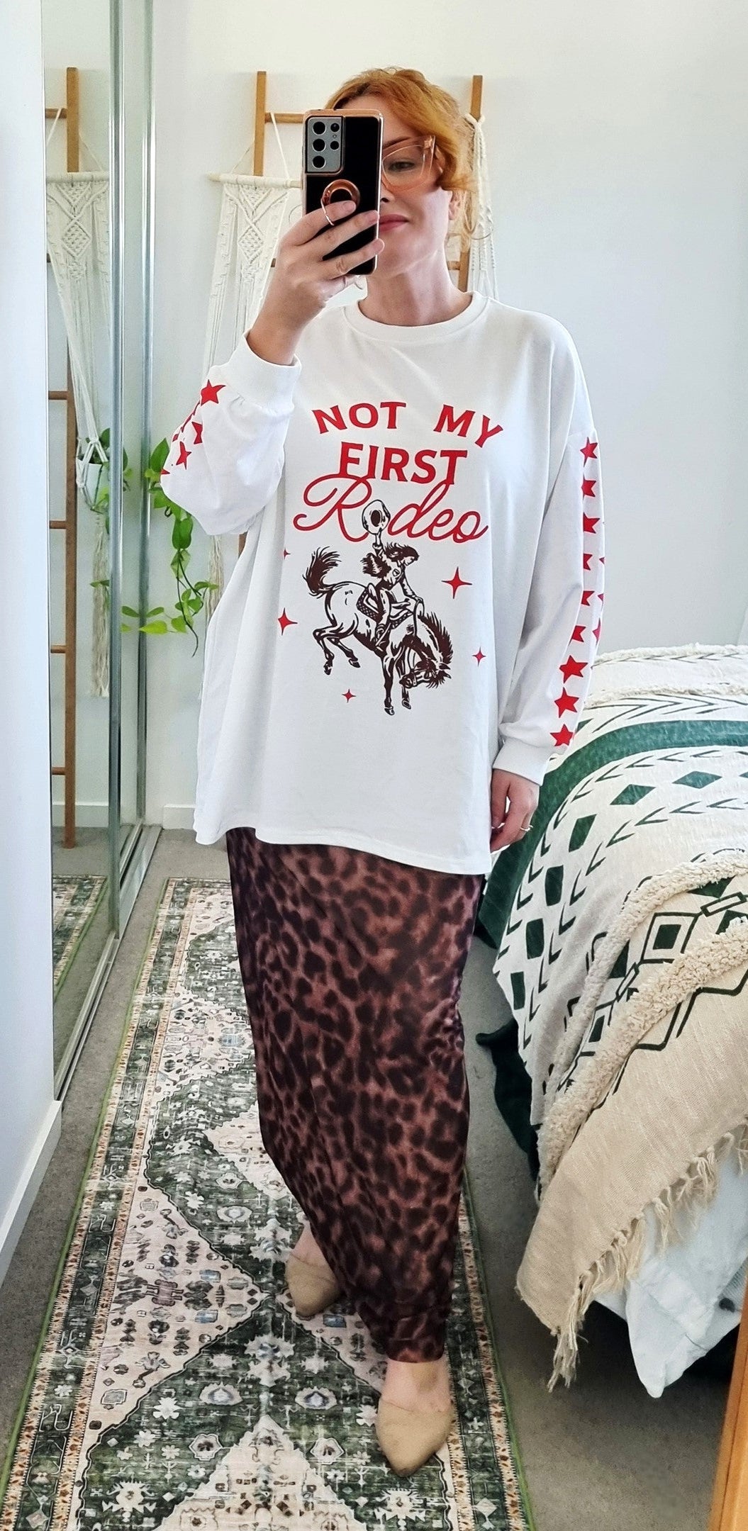 Tegan wearing the Not My First Rodeo Set by By Frankie in size Medium. Features a white oversized sweatshirt with red rodeo graphic and star-print sleeves, paired with a brown leopard-print mesh skirt. Tegan is AU size 10.